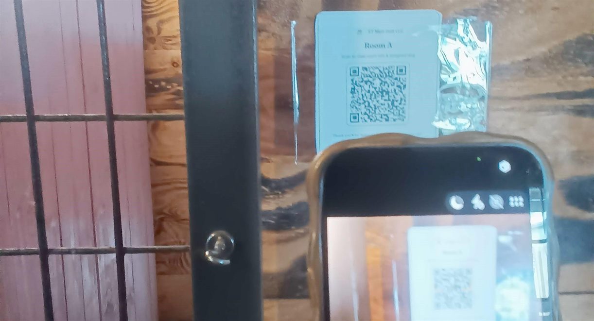 A phone camera scanning the printed room QR placard on a kennel gate